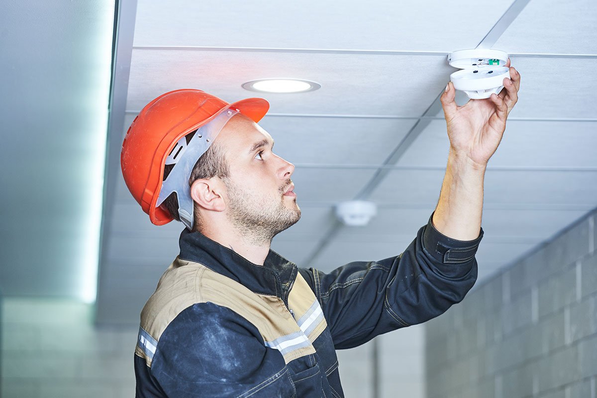 Technician inspecting a ceiling-mounted smoke detector